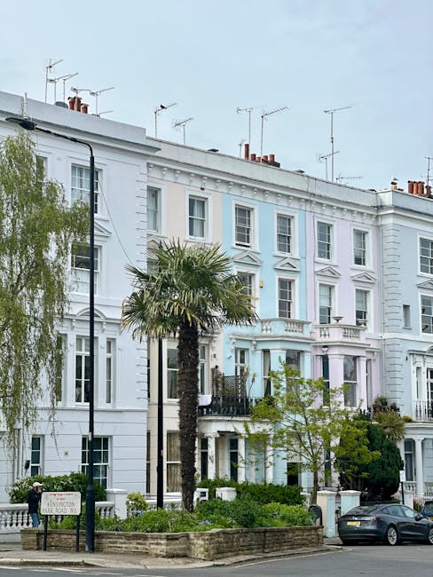A row of white Victorian-style terraced houses in Notting Hill, featuring decorative cornices and sash windows, with a small garden in front bordered by a low brick wall. In the foreground, there are