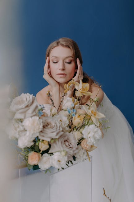 A woman with closed eyes and a serene expression holds a large floral bouquet in front of her, showcasing an arrangement of fresh, pastel-colored flowers including white roses, pale lavender blooms, c